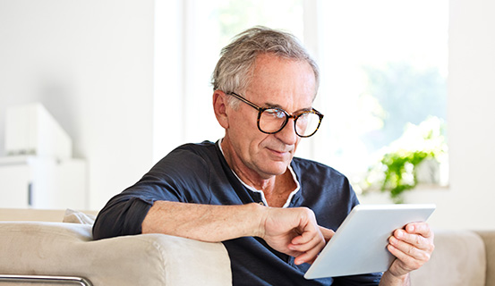 Ein Mann sitzt auf einem Sofa und hält ein Tablet in der Hand